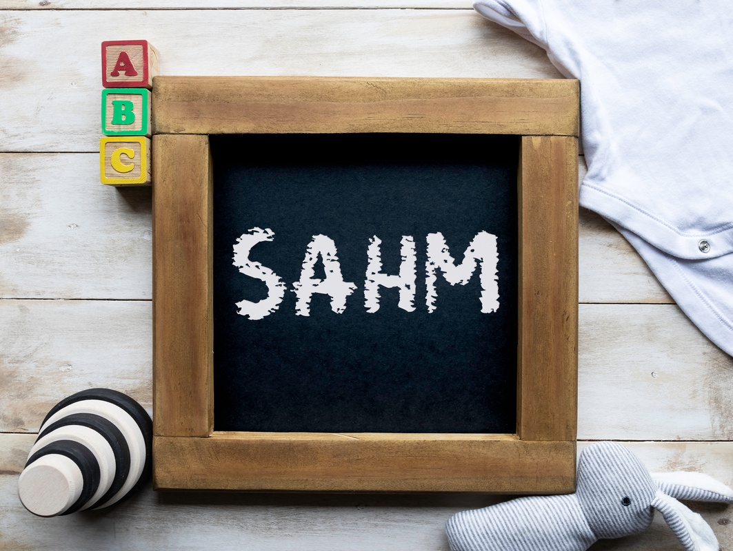 SAHM (stay at home mom/mum) message written on a chalkboard surrounded by baby toys and clothes